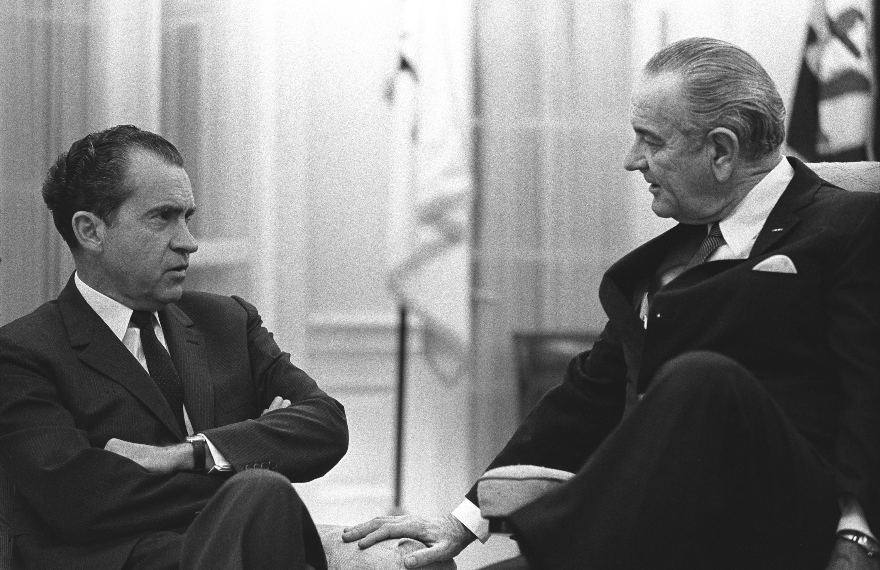 President-elect Richard Nixon sits left with arms crossed and listens to President Johnson, seated right with his legs crossed. 
